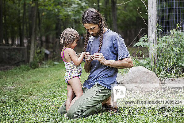 Father and daughter plaiting hair in backyard