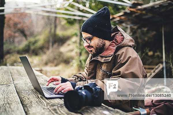 Seitenansicht eines männlichen Wanderers mit Laptop-Computer und Kamera auf einem Tisch im Wald