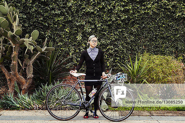 Porträt einer Geschäftsfrau  die mit dem Fahrrad vor Pflanzen steht