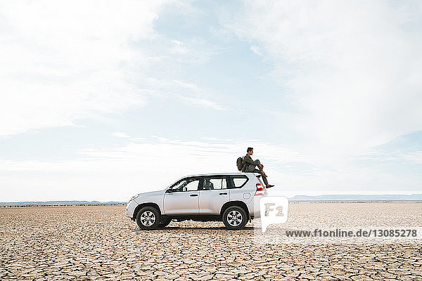 Side view of man sitting on off-road vehicle at barren landscape against cloudy sky