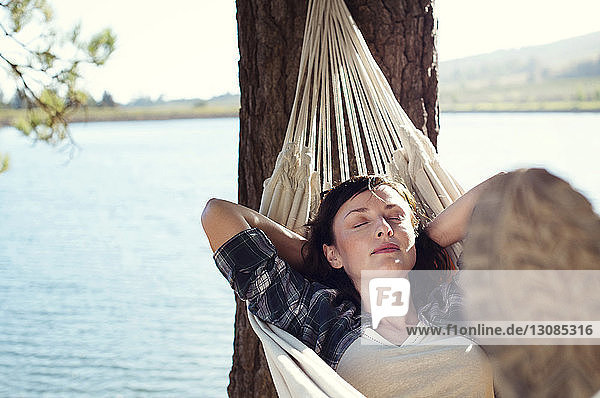 Woman sleeping on hammock at lakeshore