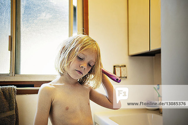 Nachdenklicher Junge ohne Hemd kämmt Haare im Badezimmer