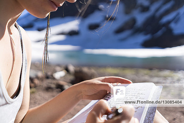 Beschnittenes Bild einer Wanderin  die auf einem Notizblock auf dem Campingplatz schreibt