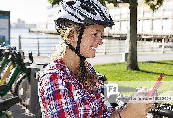 Helmtragende Frau telefoniert mit einem Helm  während sie in der Stadt gegen einen Fahrradträger steht