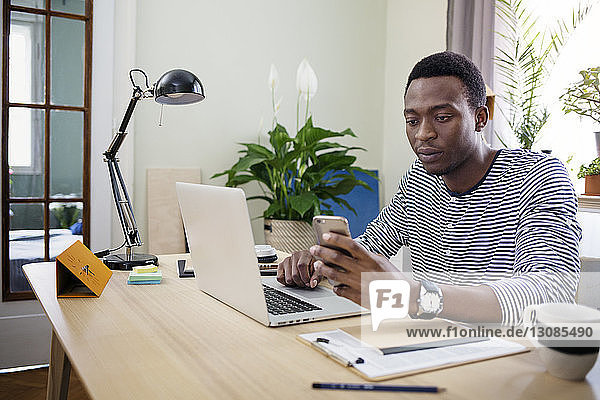 Young man using smart phone while working at home