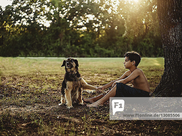 Seitenansicht eines hemdlosen Teenagers mit Hund auf dem Feld sitzend