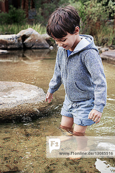 Glücklicher Junge steht im Wasser am Bach