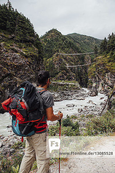 Rear view of male hiker with backpack standing by river against cloudy sky at Sagarmatha National Park
