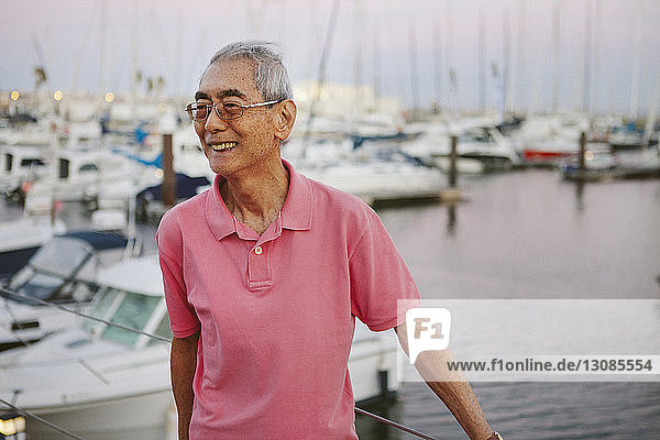 Lächelnder älterer Mann steht bei Sonnenuntergang vor im Hafen vertäuten Booten