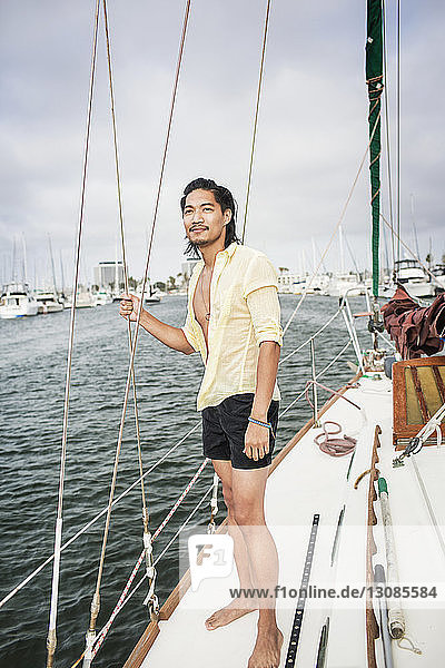 Lächelnder Mann steht an Deck eines Segelbootes gegen den Himmel