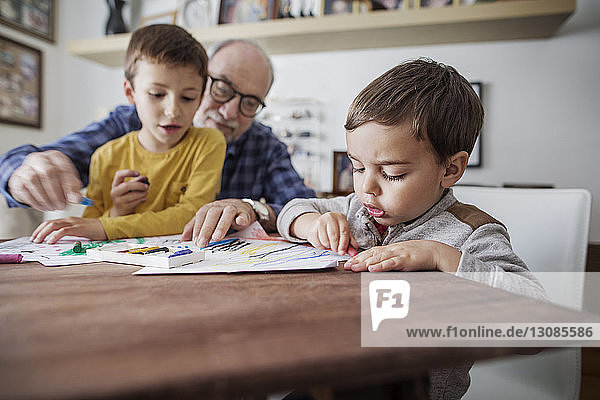 Älterer Mann hilft Enkeln beim Zeichnen zu Hause