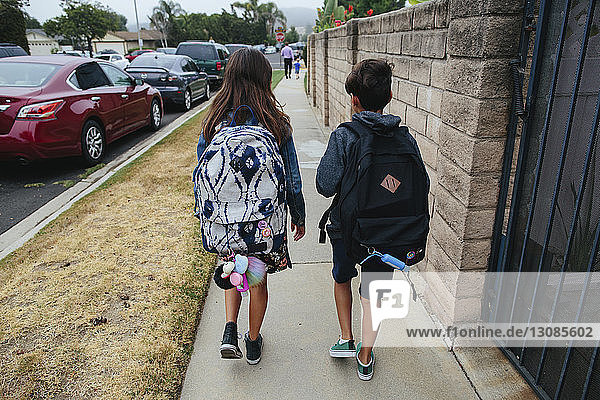 Rear view of siblings with backpack walking on footpath