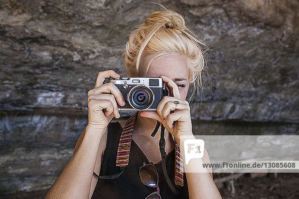Junge Frau fotografiert durch eine Oldtimer-Kamera gegen Felsen