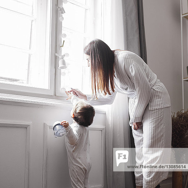 Mutter und kleiner Junge berühren Windspiel  das am Fenster im Haus hängt