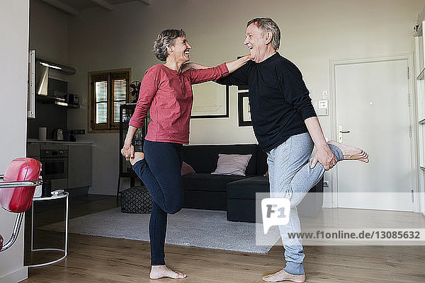 Seitenansicht eines fröhlichen Seniorenpaares,  das zu Hause Sport treibt