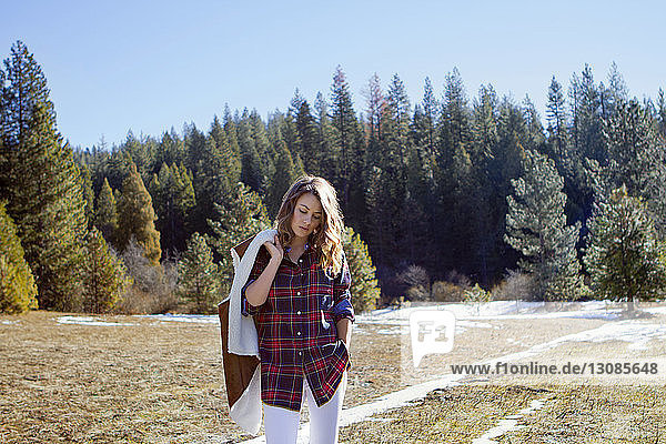 Junge Frau hält Wintermantel beim Waldspaziergang im Winter