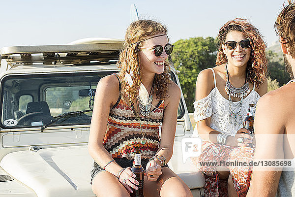 Man standing by female friends enjoying beer while sitting on off-road vehicle