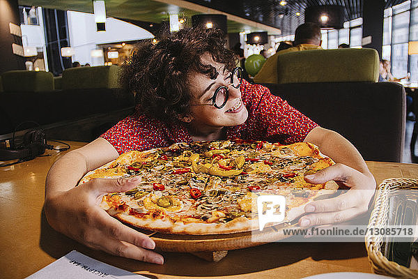 Glückliche Frau hält Pizza auf Holztisch  während sie im Restaurant sitzt