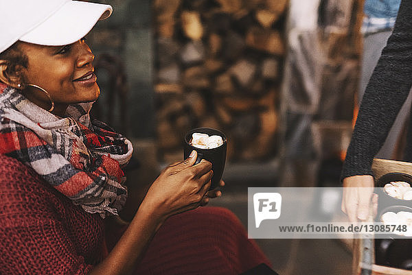 Lächelnde Frau hält Tasse  während ihr Freund Marshmallow-Getränke serviert