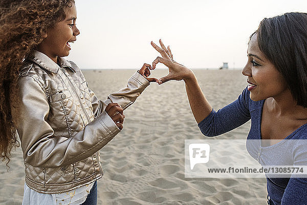 Mutter und Tochter bilden Herz mit der Hand am Strand