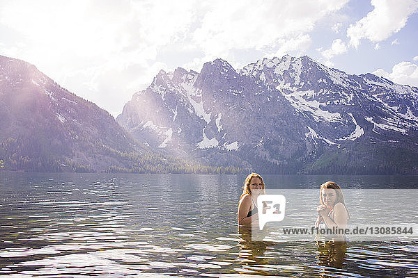 Portrait of friends swimming in lake against snowcapped mountains