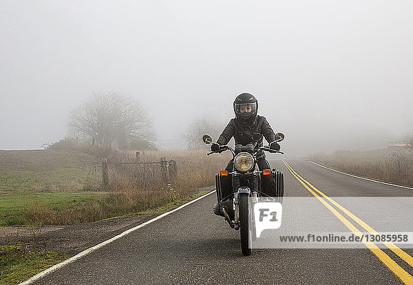 Motorrad fahrende Motorradfahrerin bei Nebel auf Landstraße