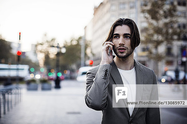 Geschäftsmann spricht mit einem Mobiltelefon  während er auf einem Fußweg in der Stadt steht