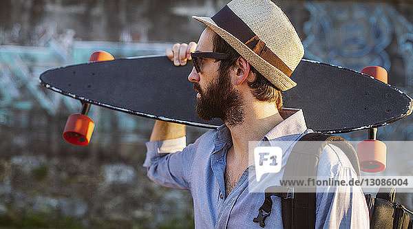 Mann mit Hut  während er Skateboard an Wand hält