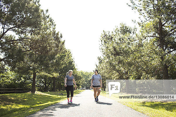 Mother and daughter in sportswear walking on footpath at park during sunny day