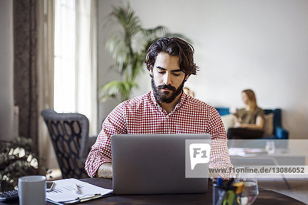 Kreativer Geschäftsmann  der am Laptop arbeitet  während er im Büro am Tisch sitzt