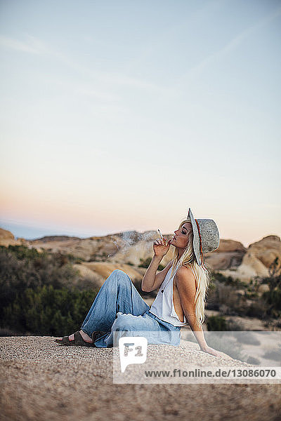 Woman smoking while sitting on rock at Joshua Tree National Park against sky