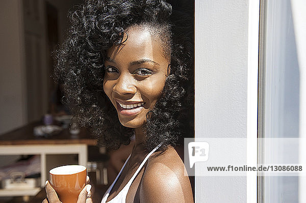 Porträt einer lächelnden Frau  die eine Kaffeetasse am Fenster hält