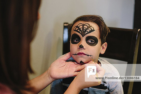 Mother applying make-up on son's face at home