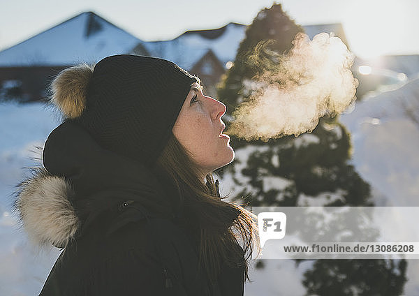 Seitenansicht einer Frau  die im Winter Atemdampf ausatmet