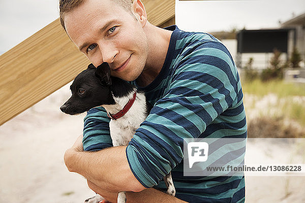 Lächelnder schwuler Mann hält Chihuahua  während er am Strand steht