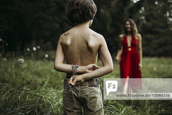 Sohn ohne Hemd hält Blumen hinter dem Rücken  Mutter im Hintergrund