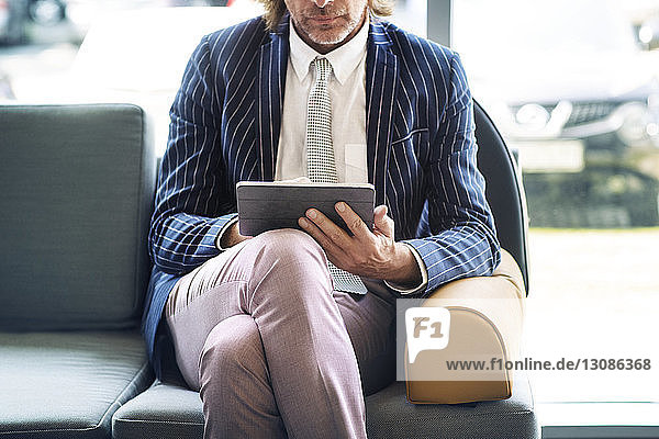 Mittelteil eines reifen Geschäftsmannes  der einen Tablet-Computer im Büro benutzt