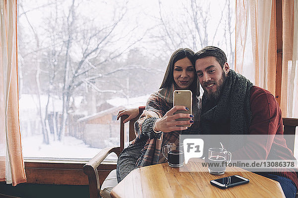 Woman with boyfriend taking selfie while sitting by window in cafe