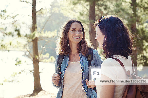 Happy female friends with backpacks standing in forest
