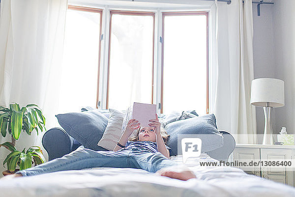 Girl reading book while lying on bed at home
