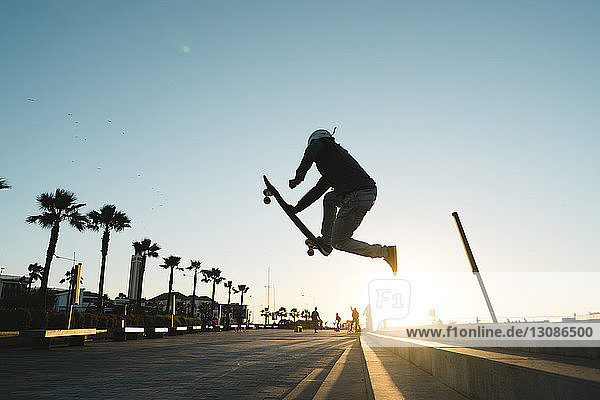 Seitenansicht eines Mannes  der einen Stunt beim Skateboardfahren auf der Straße gegen den Himmel ausführt