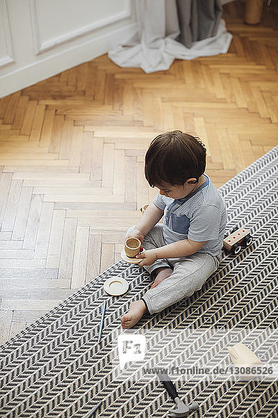 High angle view of baby boy playing with toy teacup and saucer on rug at home