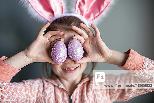 Verspieltes Mädchen mit Kaninchenohr-Stirnband  das zu Hause Ostereier hält