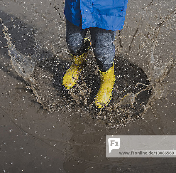 Low section of playful boy wearing rubber boots while splashing puddle