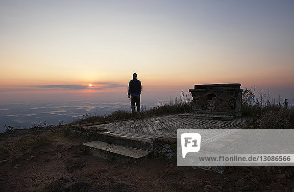 Rear view of man looking at view while standing on mountain during sunset