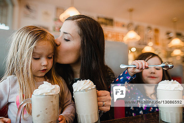 Mutter küsst Tochter beim Milchshake am Restauranttisch
