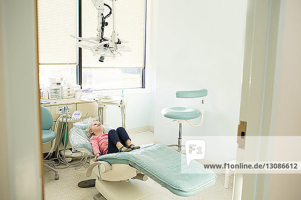 Girl lying on dentist's chair in hospital seen through doorway