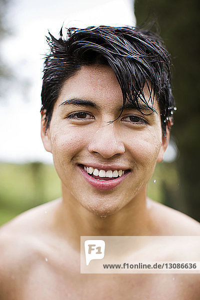 Portrait of happy shirtless man with wet hair at yard
