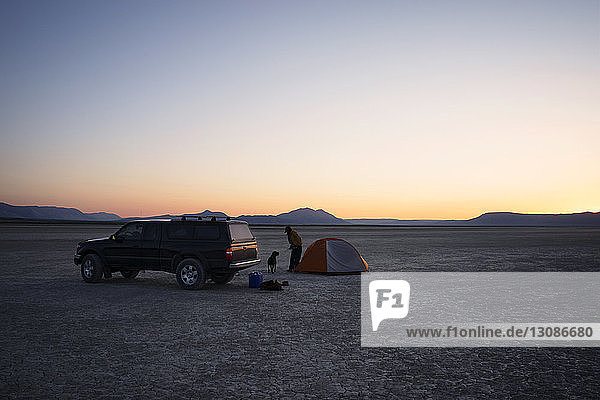 Frau und Hund stehen mit dem Auto auf dem Feld gegen den Himmel in der Alvord-Wüste