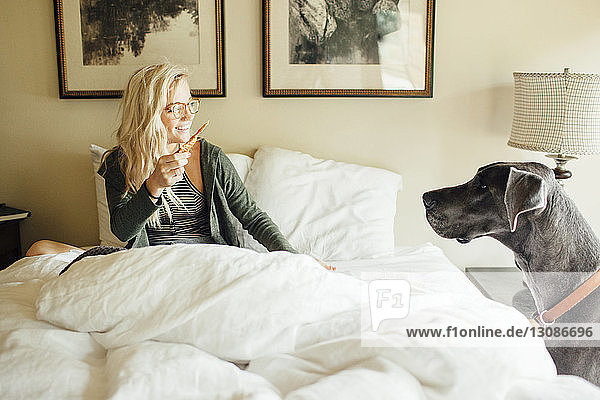 Smiling woman with food looking at Great Dane while sitting bed